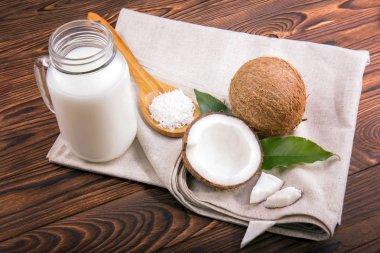 Olgun, taze, tropikal hindistancevizi meyve, parlak yeşil yaprakları ile organik hindistan cevizi sütü ve tahta kaşık fıstıklı bir ahşap arka plan üzerinde fiş.