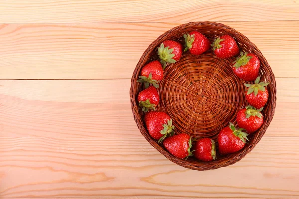 A colorful composition of a basket with fresh red strawberries forming a circle inside on a light wooden table. Healthful berries with leaves on the light background. Vegan food. — Stock Photo, Image