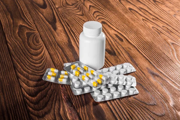 Comprimidos ou vitaminas brancas e amarelas e frasco de remédio branco fechado em uma mesa de madeira. Comprimidos, vitaminas e drogas perto de garrafa de plástico para tratamento . — Fotografia de Stock