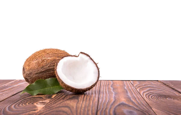 Cocos marrones brillantes de cerca con hojas verdes sobre una mesa de madera marrón oscuro, aislados sobre un fondo blanco. Un sabroso coco entero. Sabrosos cocos tropicales . — Foto de Stock