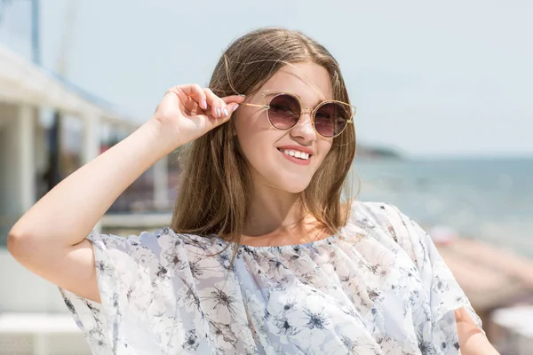 Charmante en prachtige jonge model meisje in zonnebril op de achtergrond van de zee. Een schattig vrouwelijk model. Mooi meisje in zonnebril. — Stockfoto