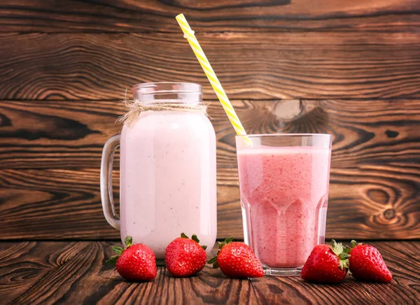 Sweet pink cocktail in a mason jar and a huge glass with a yellow straw and a lot of sweet berries around on a dark wooden background. Strawberry smoothie or milkshake. — Stock Photo, Image