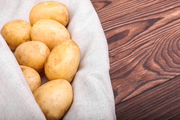 Nahaufnahme von neuen Bio-Kartoffeln auf hellgrauem Stoff und auf einem dunkelbraunen Holztisch. frische, biologische, rohe Kartoffeln. Gemüse — Stockfoto