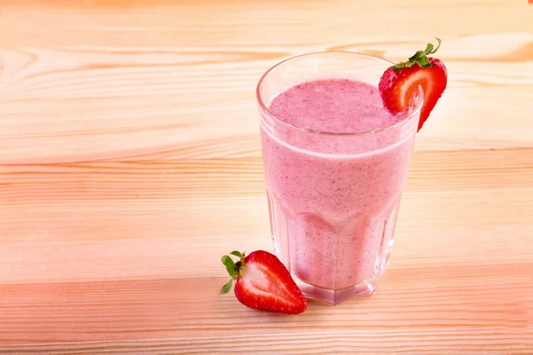 Glass of smoothie with ripe and fresh strawberries and organic milk on a light brown wooden table. Milkshake with fresh strawberries. — Stock Photo, Image