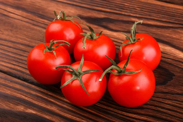 Tomates maduros y frescos con hojas verdes sobre una mesa de madera marrón oscuro. Deliciosos y jugosos tomates rojos. Cosecha de verano de verduras ecológicas . —  Fotos de Stock