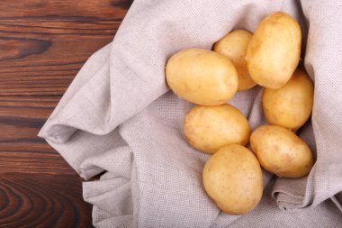 Bir sürü yeni, organik patates bir gri kumaş ve koyu kahverengi ahşap arka plan. Yaz sebze, üstten görünüm. Soyulmuş patates yumrular.