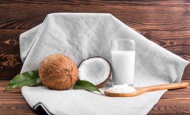 Bütün ve kesme lezzetli Hindistan cevizi ve bir bardak taze süt ve kaşık Hindistan cevizi cips koyu kahverengi ahşap masa üzerinde hafif kumaş üzerinde ile dolu bir kompozisyonun. Ödül.