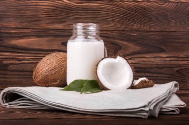 Hindistan cevizi ve gri bir ahşap zemin üzerine bez parçası üzerinde süt. Hindistan cevizi ve bir cam şişe lezzetli süt taze kesilmiş. 