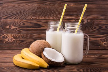 İki şeffaf mason kavanoza Hindistan cevizi sütü koyu kahverengi ahşap arka plan üzerinde dolu. Sulu sarı muz ve hindistancevizi kavanoz yakın. Taze tropikal meyve.