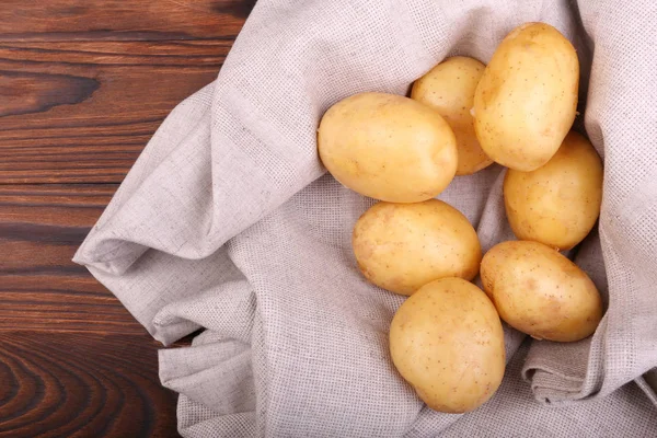Eine Menge biologischer, neuer Kartoffeln auf grauem Stoff und dunkelbraunem Holzgrund. Sommergemüse, Draufsicht. geschälte Kartoffelknollen. — Stockfoto