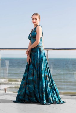 Lüks seksi elbiseli bir kadın bir güzel zümrüt ipek mavi gökyüzü arka plan üzerinde. Yaz, deniz, okyanus ve plaj kavramı. Zevk bir yaz tatili. 