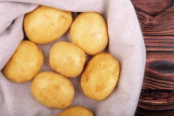 Un grand tas de jeunes pommes de terre marron clair sur un sac gris et sur un fond en bois. Beaucoup de pommes de terre crues, fraîches et non cuites sur tissu gris. Récolte estivale . — Photo