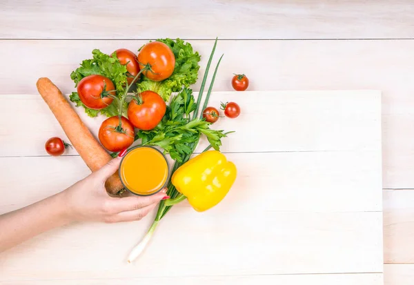 Different colorful vegetables on a wooden background. Woman holding a glass of nutritious juice. Delicious salads.