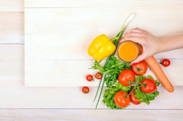 Zbliżenie warzywa na jasnym tle. Kobieta trzyma szklankę soku. Zdrowe pomidory i papryka na drewnianym stole. — Zdjęcie stockowe