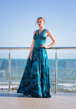 Uzun bir elbise bir çekici ve seksi genç modeli bir mavi deniz arka plan üzerinde poz. Çekici bir kadın deniz plaja yakın poz.