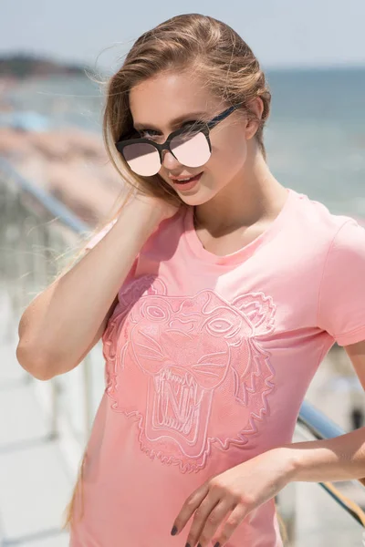 Jovem encantadora em vestido rosa e com cabelo loiro. Mulher modelo de moda bonita em óculos de sol com um sorriso bonito . — Fotografia de Stock