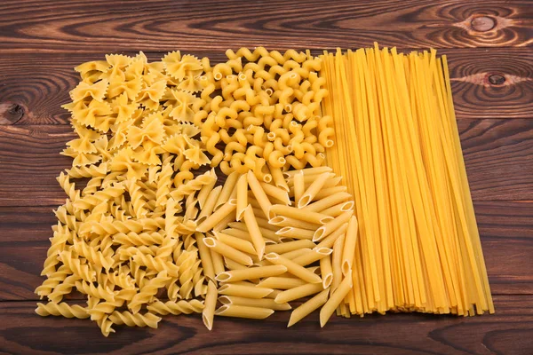 Diferentes tipos de macarrão em um fundo de madeira. Farfalle, fettuccine, macarrão, fusilli e penne rigate. Cozinha italiana saborosa . — Fotografia de Stock