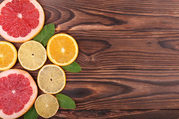 Rebanadas multicolores de jugosa naranja, limón maduro y pomelo fresco con hojas de color verde brillante en una mesa de madera marrón oscuro, vista superior. Vitamina C . — Foto de Stock