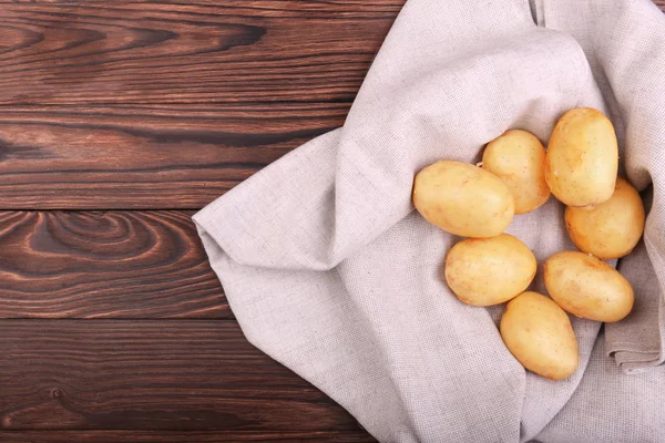 Beaucoup de pommes de terre crues et jeunes sur un sac gris clair et sur un fond de bois brun foncé. Pommes de terre crues, propres et fraîches avec une peau fine . — Photo