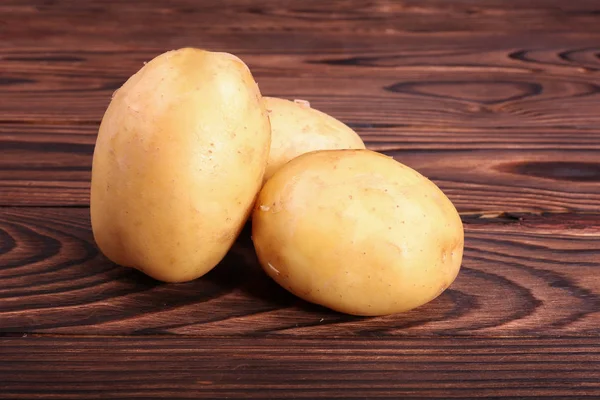 Rohe, frische und ungekochte Kartoffeln auf dunkelbraunem Holzgrund. frisches Gemüse. natürliche pflanzliche, frische landwirtschaftliche Lebensmittel. rohe, saubere und hellbraune neue Kartoffeln. — Stockfoto