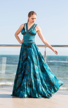 Mavi gökyüzü arka plan üzerinde güzel bir zümrüt elbiseli şık bir kadın. Bir teras üzerinde uzun boylu ve sıska bir kız. Lüks konsepti.