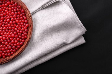 Siyah bir zemin üzerine kırmızı kuş üzümü doymuş. Bir sepet gri kumaş üzerine kırmızı kuş üzümü dolu. Sağlıklı yemekler için rustik çilek.