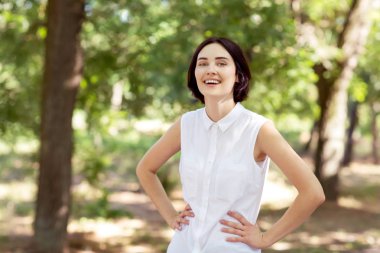 Güneşli park arka plan üzerinde mutlu bir kadın. El HIPS kendine güvenen bir kadınla. Profesyonel bir işçi dışında. Başarı kavramı. 