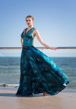 Mavi gökyüzü arka plan üzerinde uzun sallayarak bir zümrüt elbiseli güzel bir kadın tam uzunlukta portresi. Kadınlık, uyum kavramı.