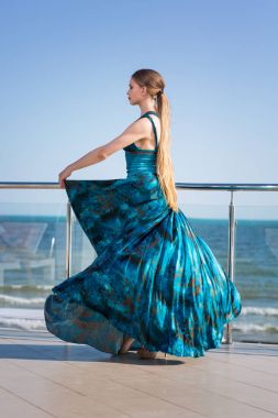 Parlak mavi deniz arka plan üzerinde turkuaz elbiseli şık bir kız. Genç bayan bir otelin Cam Balkonda kalıyor. 