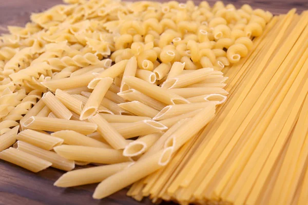Una varietà di tipi e forme di pasta secca italiana su uno sfondo di legno. Pasta cruda, dura, cruda e secca. maccheroni saporiti secchi . — Foto Stock