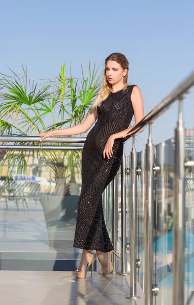 Uma mulher bonita e glamourosa em um vestido elegante em um terraço do hotel chique. O modelo maravilhoso em um fundo azul céu . — Fotografia de Stock