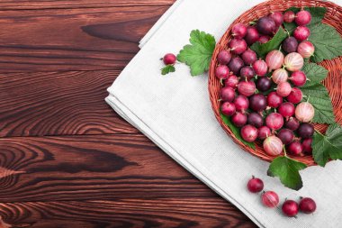 Ahşap bir masa üzerinde hafif kahverengi sepet içinde yeşil yaprakları ile çok renkli bektaşi sağlıklı, taze, olgun. Bektaşi tonlarını parlak kırmızı renk.