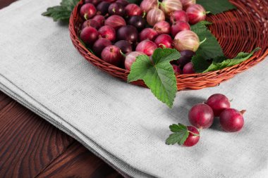 Çok renkli bektaşi gri kumaş üzerinde ve ahşap arka plan üzerinde kahverengi ahşap sepet. Yakın çekim olgun taze kırmızı meyveler. Lezzetli meyveler.