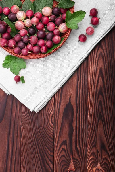 Close-up picture of ripe bright red gooseberries in a basket on a gray bag and wooden table. Gooseberries different shades of bright red color.