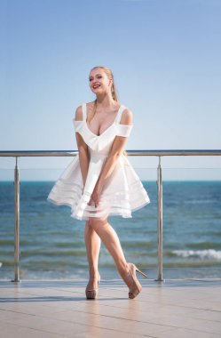 Bir otelin terasında poz harika bir bayan. Parlak gökyüzü arka plan üzerinde gülümseyen kadın. Kısa beyaz elbiseli şık kız.