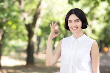 Renkli bir parkta beyaz bir gömlek gülümseyen kendinden emin ve genç kadın. Mutlu kız 