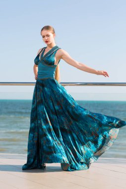 Mavi denize yakın poz bir zarif Bayan uzun sarı at kuyruğu ve bir uzun sallayarak zümrüt elbiseli. Denizde tatil kız güzel.