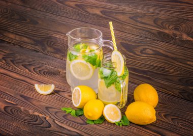 Limon suyu ile bir büyük cam sürahi, uzun sarı saman ve koyu kahverengi ahşap kürsüye limon ile bir bardak, beyaz bir arka plan üzerinde tablo izole. 