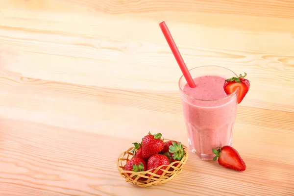 Little basket full of strawberries is standing on a desk next to the transparent glass of delish coral smoothie with a scarlet straw. — Stock Photo, Image