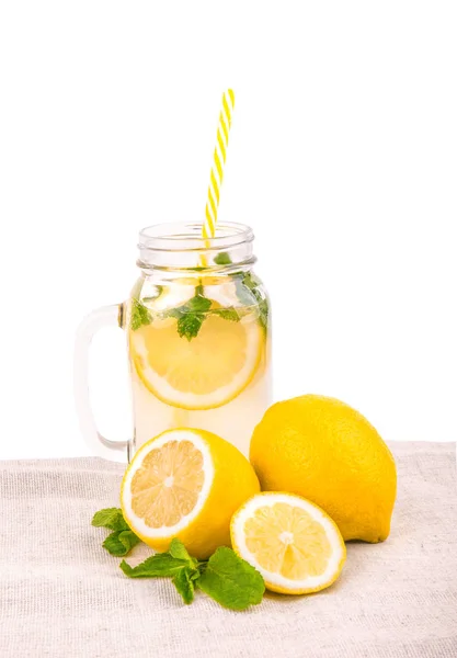 Um jarro com suco de limão e limões em um tecido leve, isolado em um fundo branco. Uma palha amarela longa e fatias de limão em um grande pote com limonada . — Fotografia de Stock