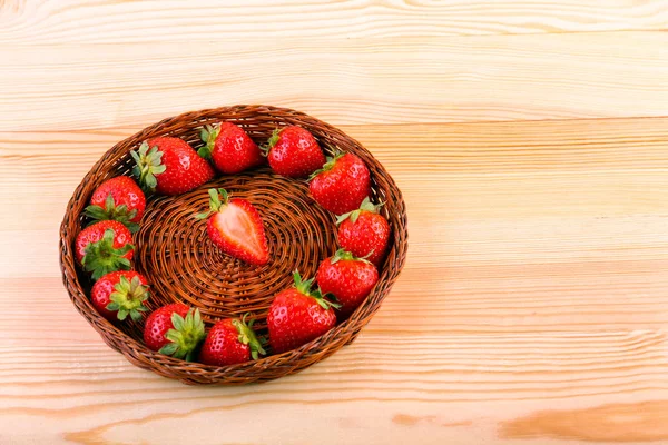 A colorful composition of a dark brown basket is standing on a light wooden table with fresh red healthy strawberries are lying inside, forming a circle. — Stock Photo, Image