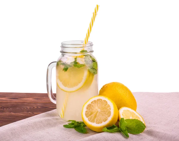 Μια σύνθεση από ένα γυάλινο βάζο με ένα κίτρινο Καλαμάκι και κίτρινο ώριμα και ζουμερά ποτά με θρυμματισμένο πάγο και πράσινο φρέσκο δυόσμο σε τραπέζι καφέ, απομονώνονται σε λευκό φόντο. — Φωτογραφία Αρχείου
