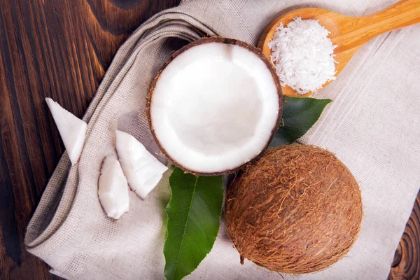 Widok z góry kokosów i łyżką z płatków na tkaninę. Pęknięty kokosy z liści na tle drewnianych. Słodkie desery. — Zdjęcie stockowe
