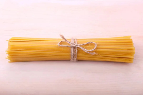 Massa bonita com um pouco de corda em forma de laço. Macarrão de massa amarela sobre um fundo de madeira brilhante. Cozinha mediterrânica . — Fotografia de Stock