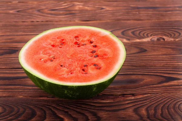 Una sandía madura, jugosa y deliciosa cortada por la mitad sobre un fondo de madera marrón oscuro. La pulpa de sandía es dulce y la corteza verde . — Foto de Stock