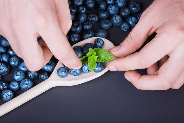 Man's hands doing a composition with fresh berries around a spoon, top view.  Top view of blueberries on a dark background.