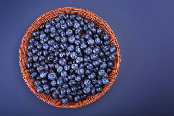 Una canasta de madera con arándanos jugosos y amargos sobre un fondo púrpura oscuro. Bayas frescas y maduras de color azul brillante, vista superior. Una caja llena de bayas . — Foto de Stock