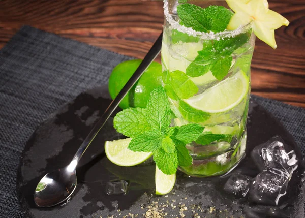 Refreshing mojito with rum, fresh lime, mint, crushed ice and carambola on a dark wooden background. Summer and alcohol beverage. — Stock Photo, Image
