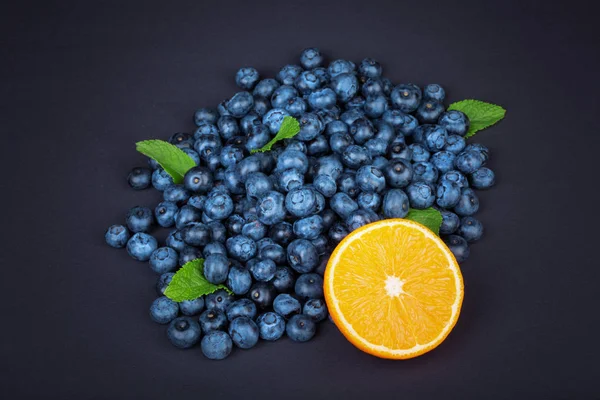 Arándanos dulces con la mitad madura de menta naranja y verde. Arándanos enteros, orgánicos y jugosos con la mitad de naranja y menta sobre un fondo oscuro . — Foto de Stock