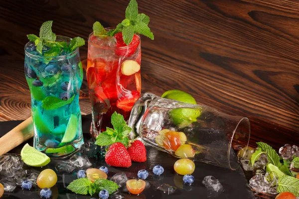 Цветные коктейли с мятой, лаймом, льдом, ягодами на деревянном фоне. Освежающие летние напитки. Копирование пространства . — стоковое фото